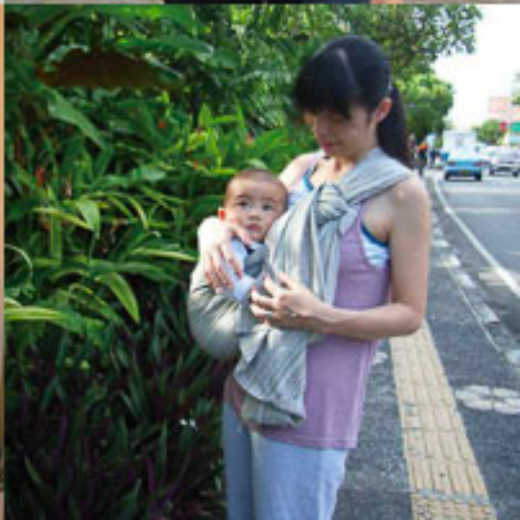 緑の植物の前で、ストライプのスリングに赤ちゃんを抱く女性