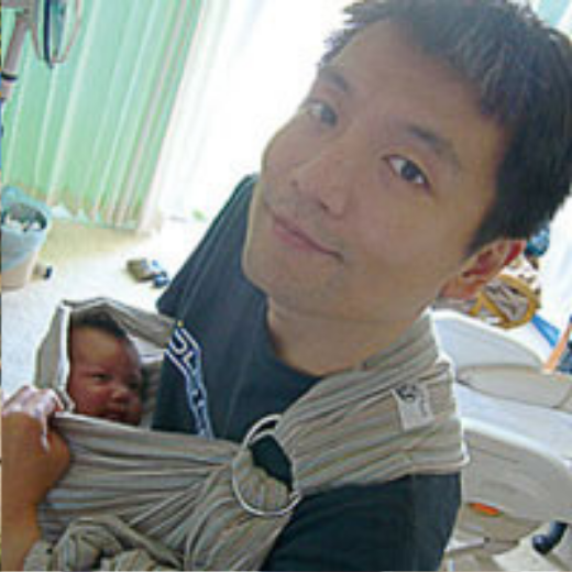自宅で赤ちゃんをスリングに入れて優しく抱くパパ