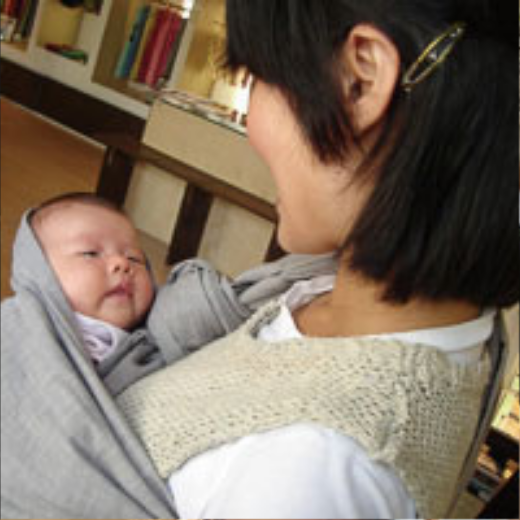 室内でスリングに包まれた赤ちゃんと見つめ合うお母さんの横顔