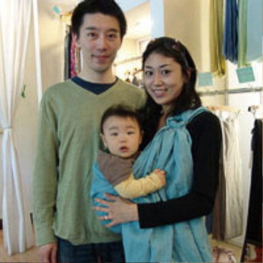 青色のスリングに赤ちゃんを抱いた母親と、その隣で寄り添う父親の家族写真。
