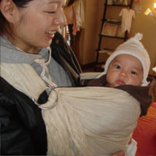 生成りのスリングで帽子をかぶった赤ちゃんを抱くママ