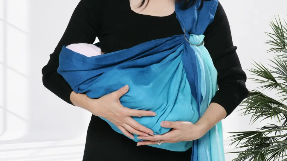 ピースリングを装着して赤ちゃんを抱く女性の上半身写真。テキスト「やさしく、確かに抱きしめる。正しい使い方で、心地よい抱っこを。How to Use | Manuals for PsLing」が重ねられている。